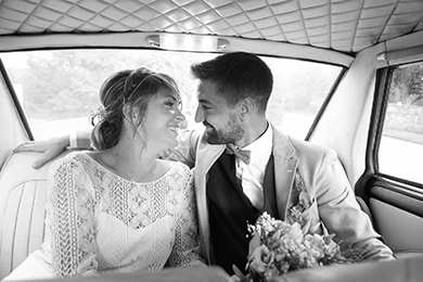 Photo en noir et blanc de mariés sur le point de s'embrasser dans une voiture.